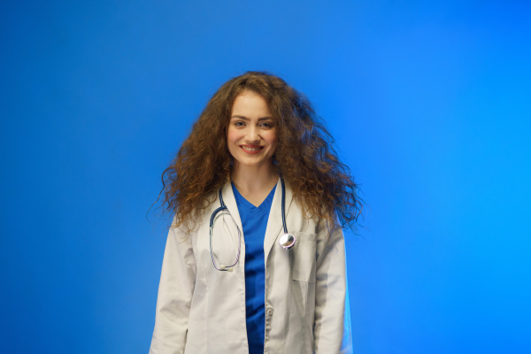 A studio shot of a young female doctor looking at camera against a blue background.