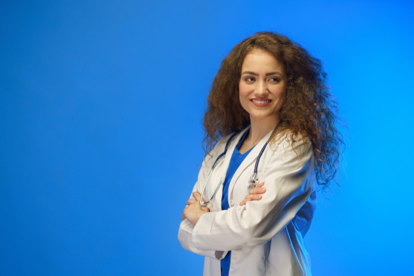 A studio shot of a young female doctor looking at camera against a blue background.