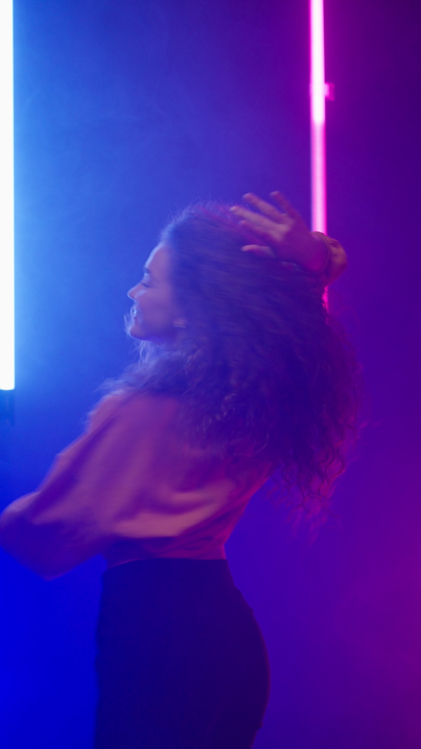 A happy young woman dancing over neon light background at disco party