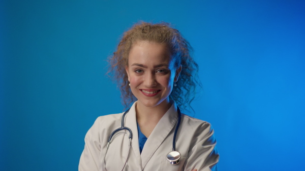 Young female doctor smiling and looking at camera against blue background.