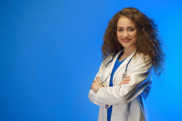 A studio shot of a young female doctor looking at camera against a blue background.