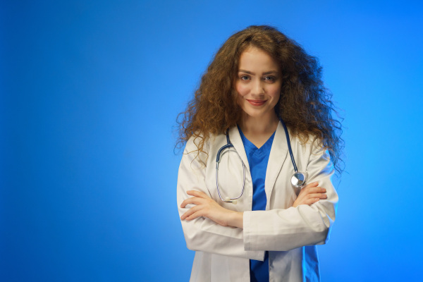 A studio shot of a young female doctor looking at camera against a blue background.