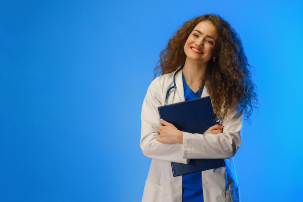 A studio shot of a young female doctor looking at camera against a blue background.