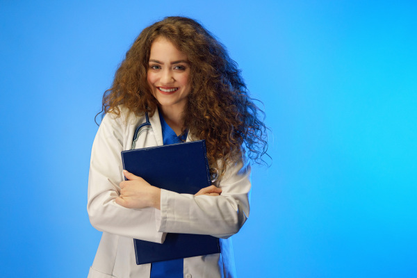 A studio shot of a young female doctor looking at camera against a blue background.