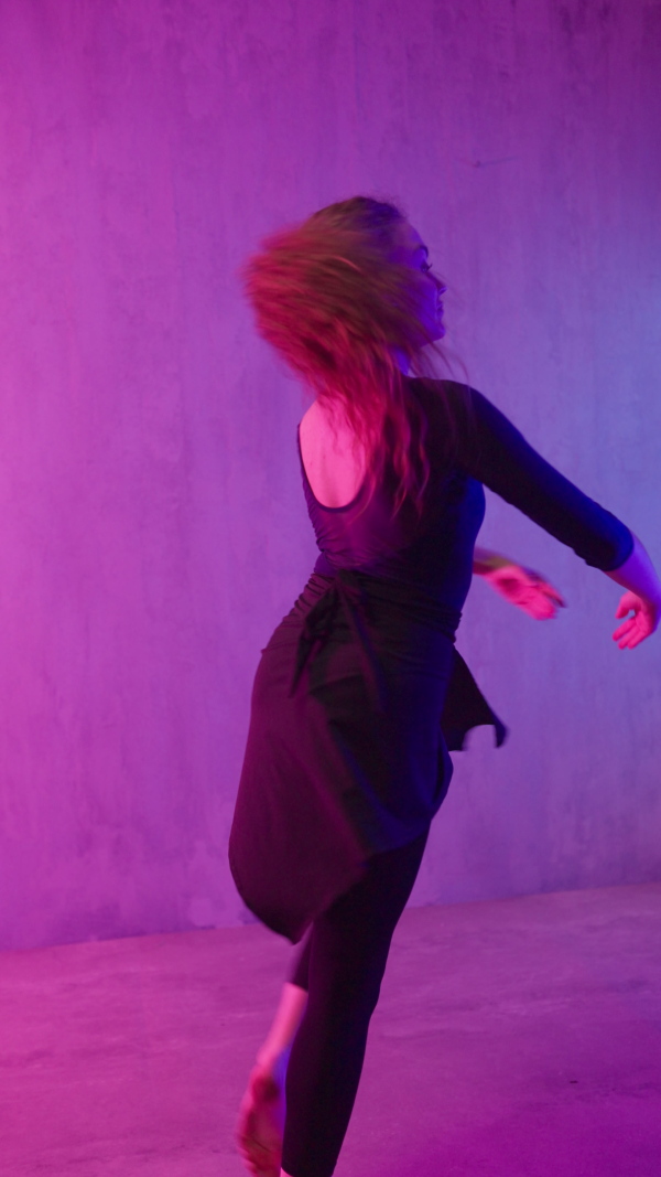 A happy young woman dancing over neon light background at disco party