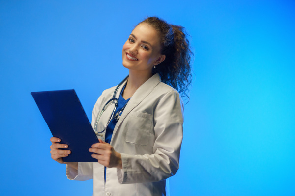 A studio shot of a young female doctor looking at camera against a blue background.