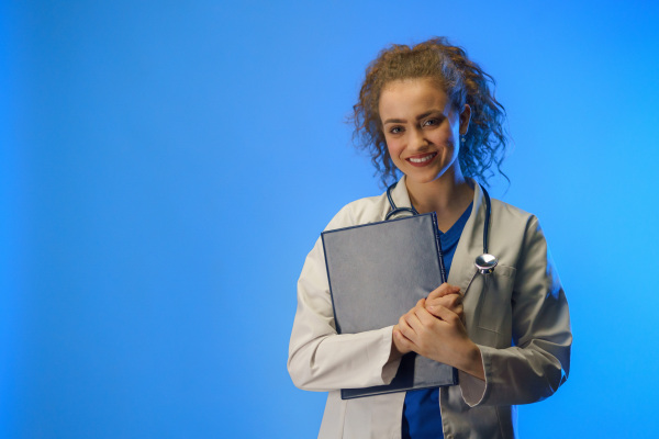 A studio shot of a young female doctor looking at camera against a blue background.