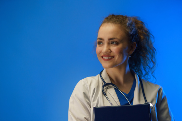 A studio shot of a young female doctor looking at camera against a blue background.