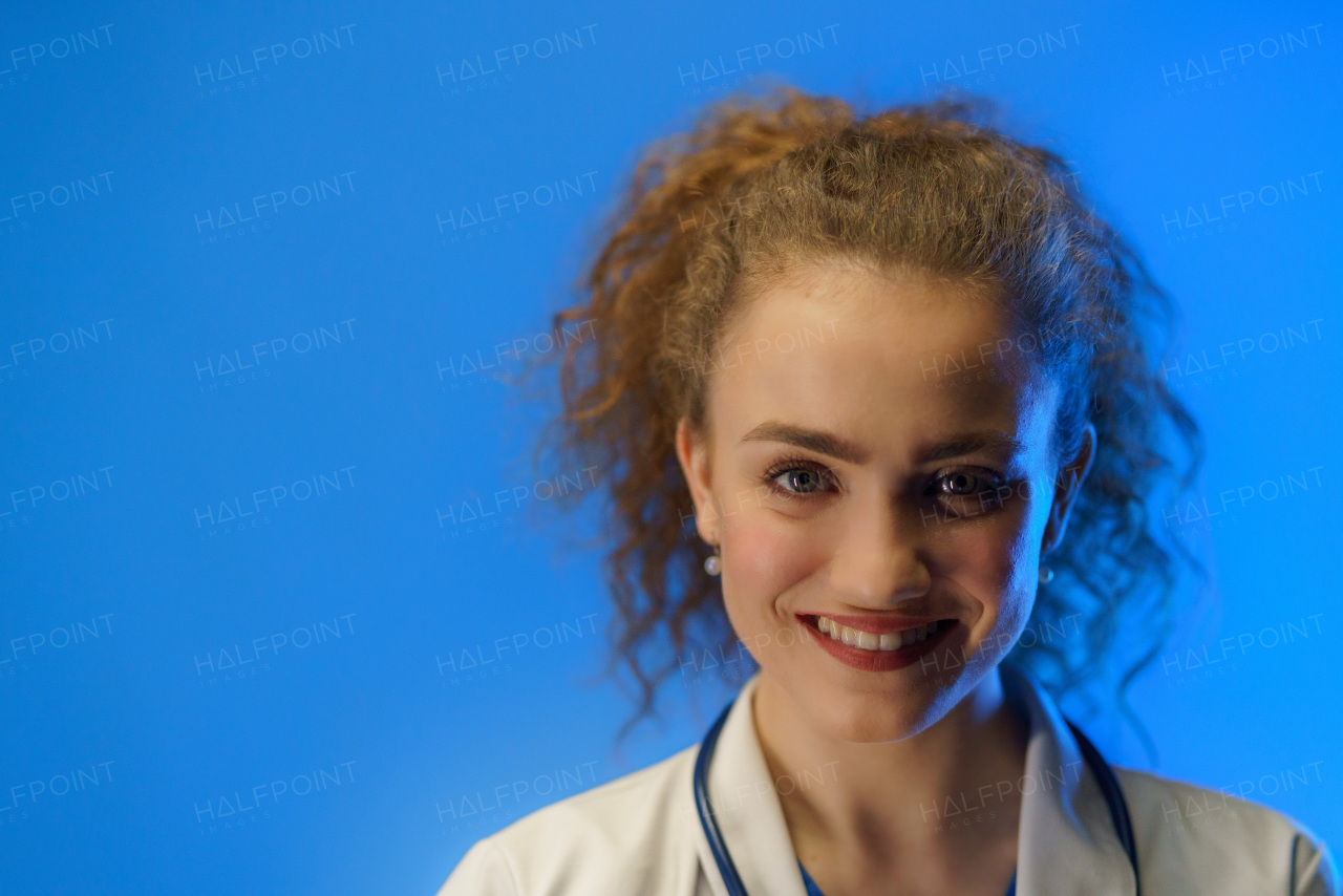 A studio shot of a young female doctor looking at camera against a blue background.