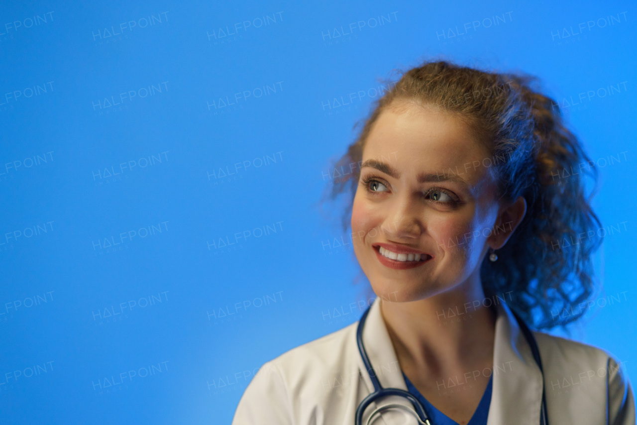 Portrait of a young female doctor with a stethoscope against a blue background.