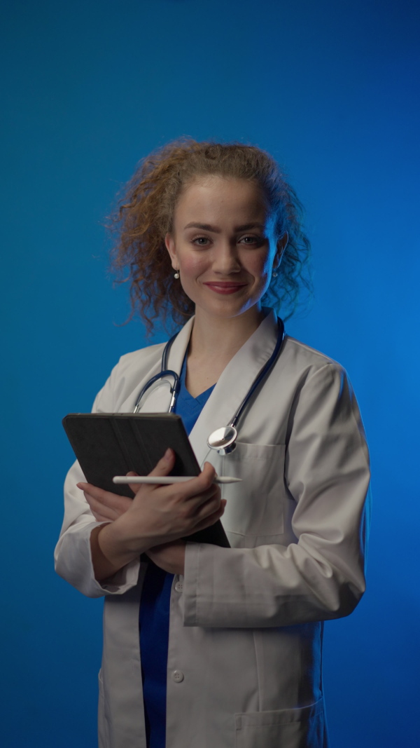 Young female doctor smiling and looking at camera against blue background.