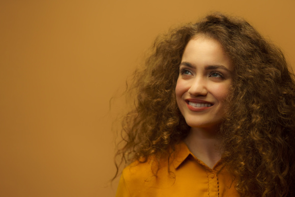 Studio portrait of a young happy woman looking at the distance,yellow background, copy space.