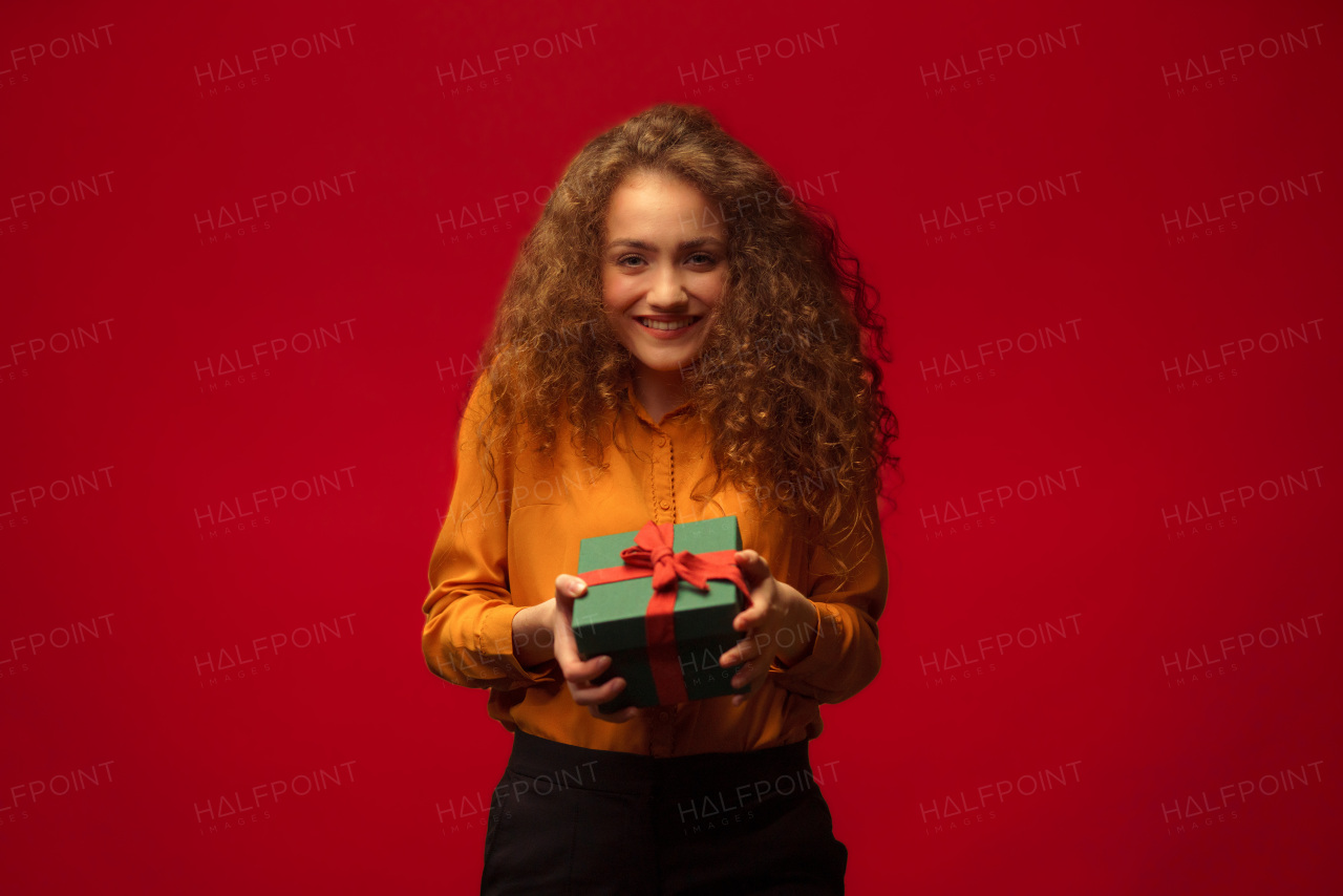 Portrait of happy young woman holding a gift box, red background.