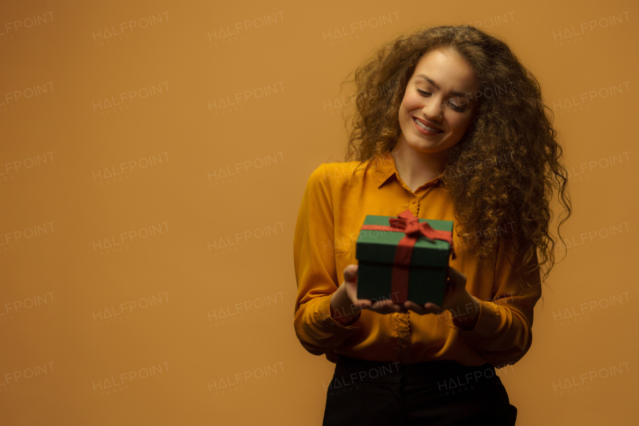 Portrait of happy young woman holding a gift box, orange background.