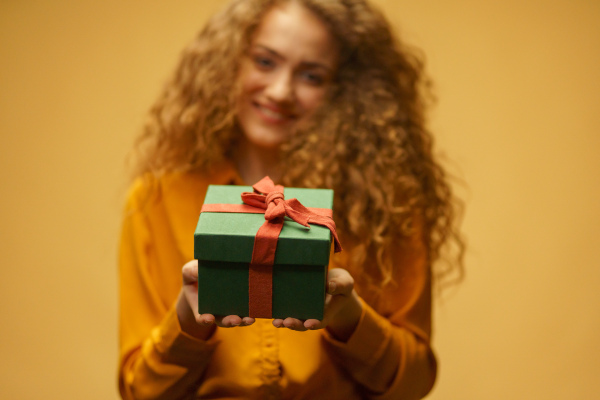 Happy young woman giving gift box iver yellow background.