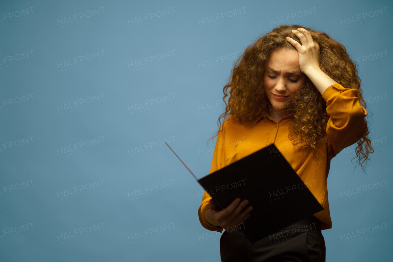 A studio portrait of worried businesswoman holding folder and papers, on grey background.