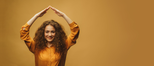 A photo portrait of woman making roof over head with hands isolated on bright yellow colored background. Life insurance concept.