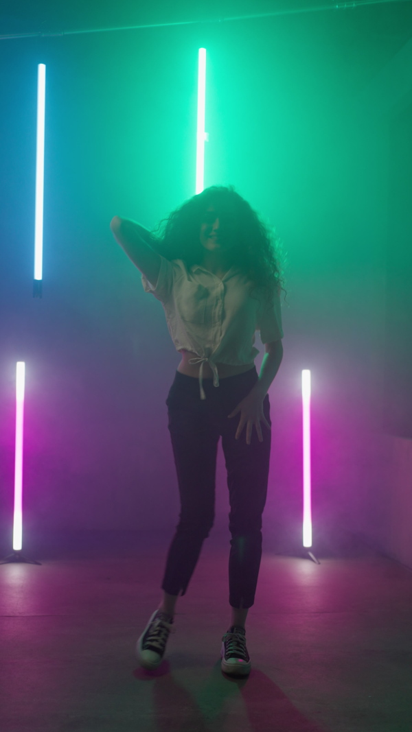 A happy young woman dancing over neon light background at disco party