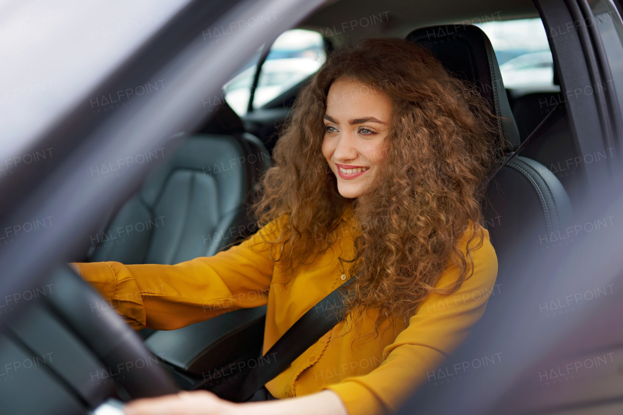 A young woman driving a car in the city. Portrait of a beautiful woman in a car, looking out of the window and smiling.