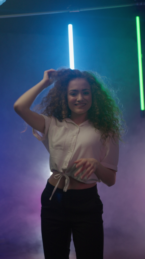 A happy young woman dancing over neon light background at disco party