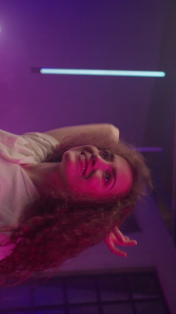 A happy young woman dancing over neon light background at disco party