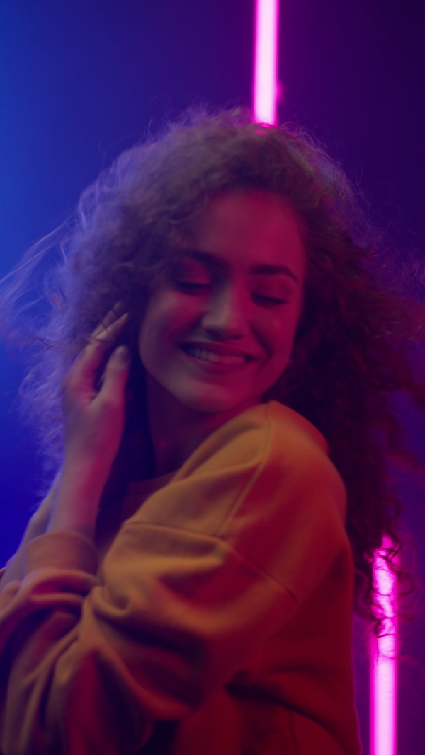 A happy young woman dancing over neon light background at disco party