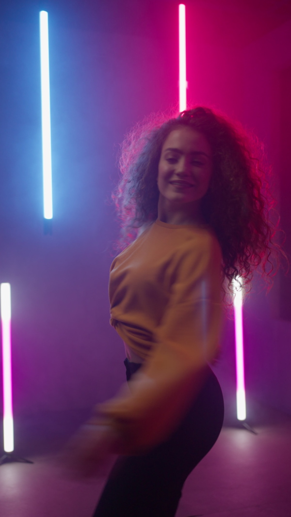 A happy young woman dancing over neon light background at disco party