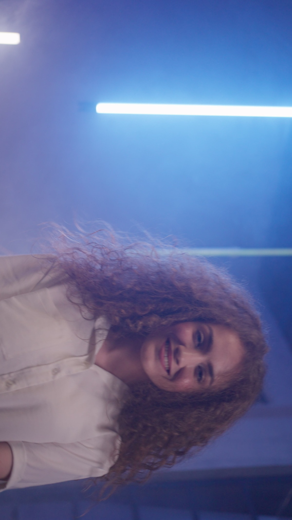 A happy young woman dancing over neon light background at disco party