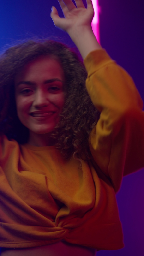 A happy young woman dancing over neon light background at disco party