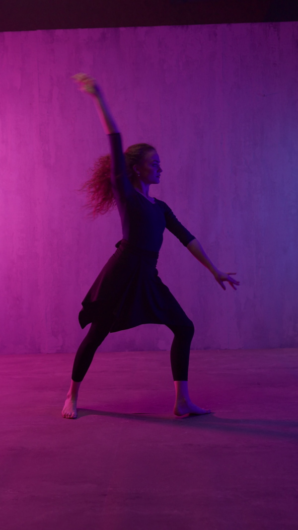 A happy young woman dancing over neon light background at disco party