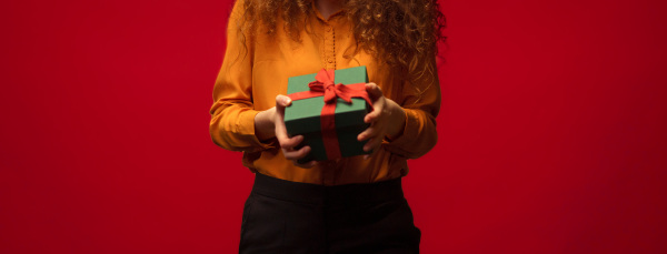 Close-up of young woman holding a gift box, red background.