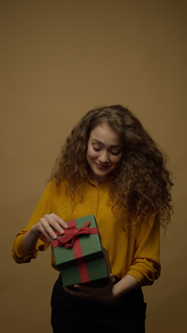 Happy young woman getting a gift box and opening it, yellow background.