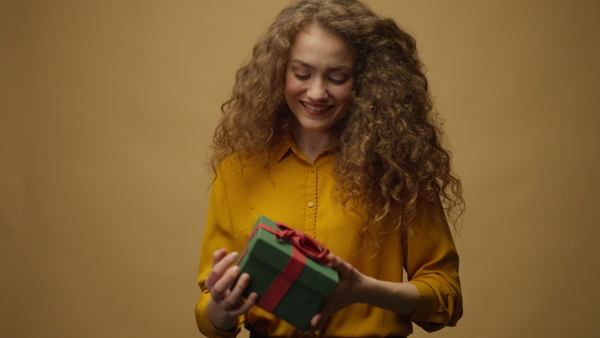 Happy young woman getting a gift box and opening it, yellow background.