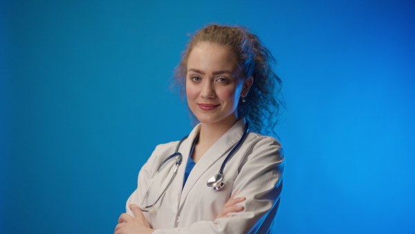 Young female doctor smiling and looking at camera against blue background.