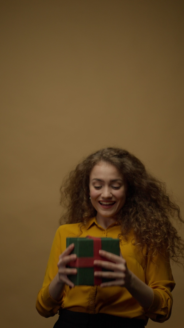 Happy young woman getting a gift box and opening it, yellow background.