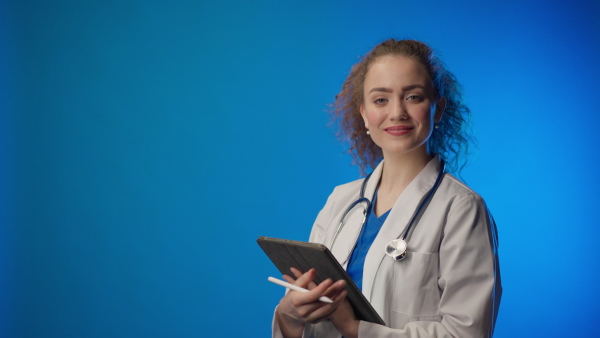 Young female doctor smiling and looking at camera against blue background.