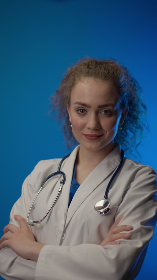 Young female doctor smiling and looking at camera against blue background.