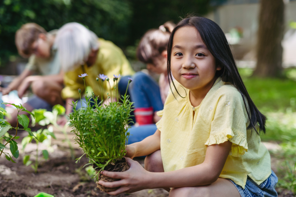 Portrait of cute schoolgirl taking care of plants in school garden during at outdoor sustainable education class.Concept of experiential learning, ecoliteracy.