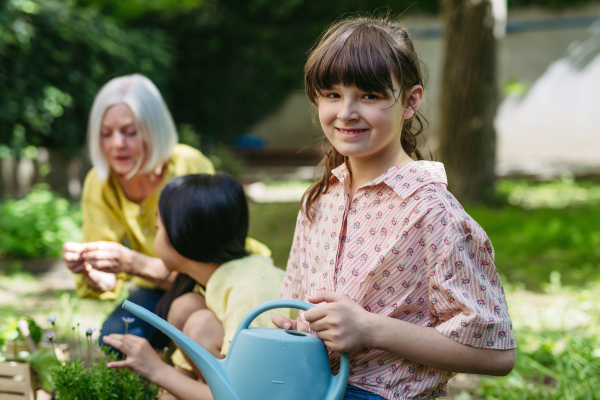 Portrait of cute schoolgirl taking care of plants in school garden during at outdoor sustainable education class.Concept of experiential learning, ecoliteracy.