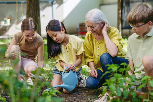 Young kids taking care of plants in school garden during at outdoor sustainable education class, planting flowers, herbs and vegetables. Concept of experiential learning, ecoliteracy.