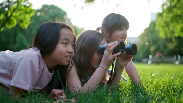 Young girl students learning about nature and wildlife in urban environment, using binoculars and observing animals, birds in public park.