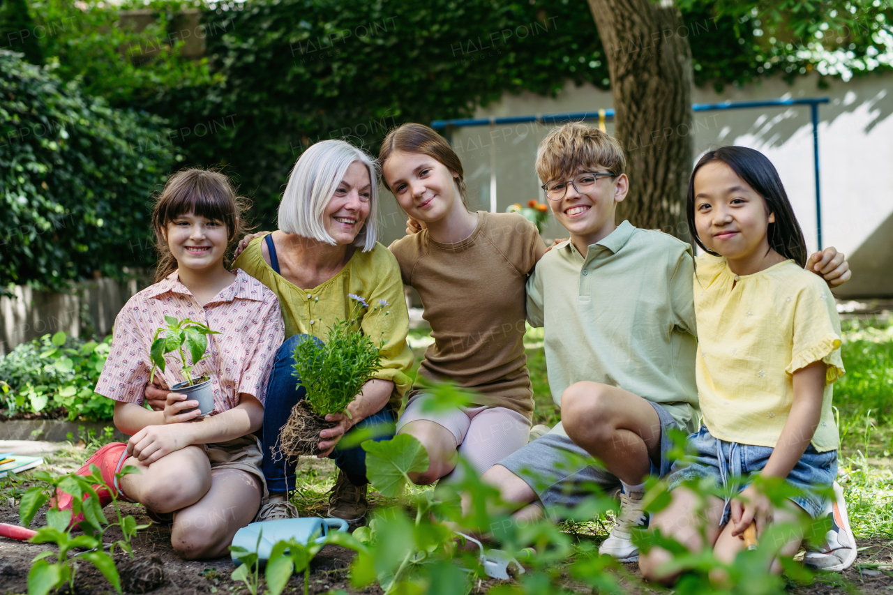 Portrait of students and female teacher at outdoor sustainable education class. Planting vegetable seedling, herbs in soil. Concept of experiential learning, ecoliteracy.