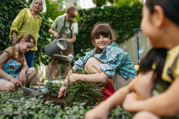 Students and female teacher at outdoor sustainable education class. Kids taking care of plants in school garden. Concept of experiential learning, ecoliteracy.