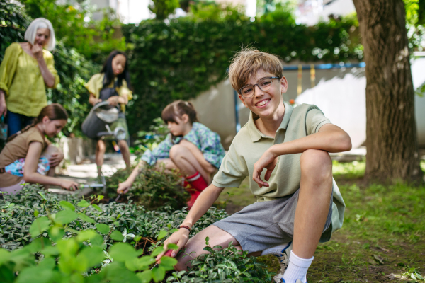 Students and female teacher at outdoor sustainable education class. Kids taking care of plants in school garden. Concept of experiential learning, ecoliteracy.