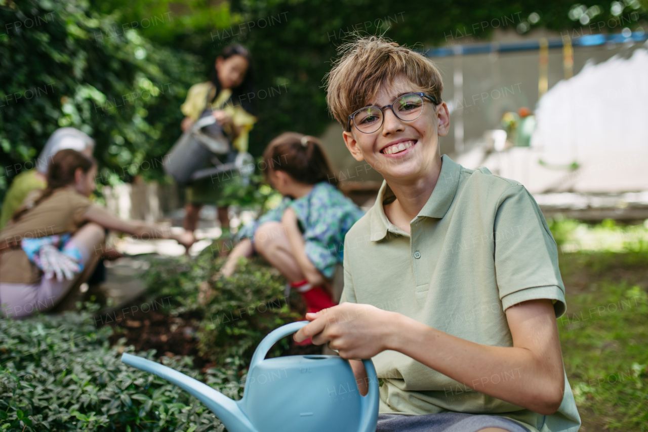 Portrait of schoolboy taking care of plants in school garden during at outdoor sustainable education class.Concept of experiential learning, ecoliteracy.