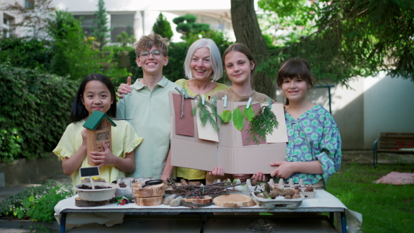 Insect hotel as educational tool for children in outdoor sustainable educational class. Young students learning about insect and biodiversity, holding wooden bug house.