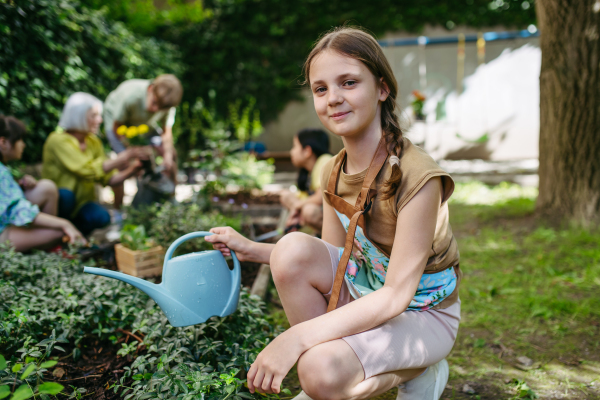 Portrait of cute schoolgirl taking care of plants in school garden during at outdoor sustainable education class.Concept of experiential learning, ecoliteracy.