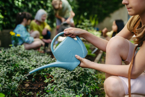 Schoolgirl watering plants in school garden during at outdoor sustainable education class.Concept of experiential learning, ecoliteracy.