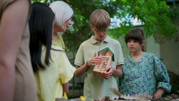 Insect hotel as educational tool for children in outdoor sustainable educational class. Young students learning about insect and biodiversity, holding wooden bug house.