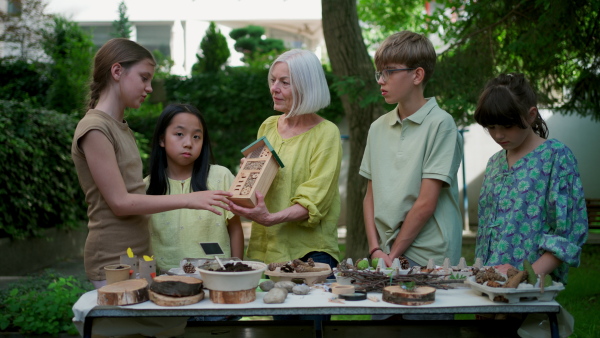 Insect hotel as educational tool for children in outdoor sustainable educational class. Young students learning about insect and biodiversity, holding wooden bug house.